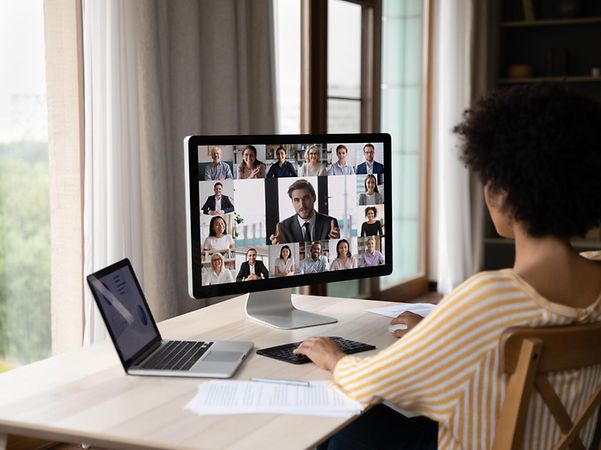 A woman is sitting in front of a screen, talking to four colleagues via video conference.