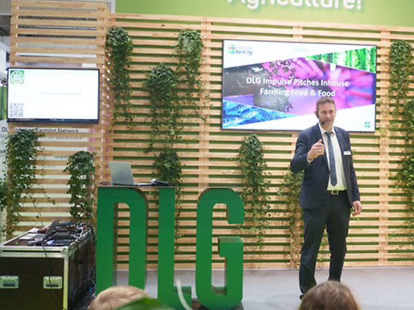 A person is giving a presentation on stage, with digital agriculture-related images in the background.