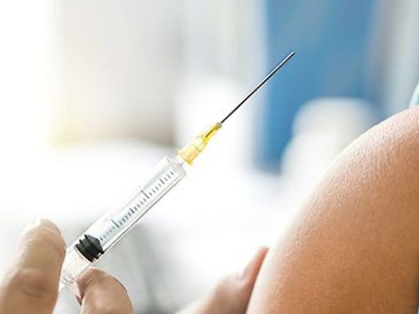 A syringe is being prepared for a vaccination on a person’s upper arm.