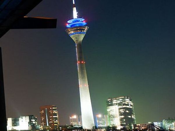 The illuminated Rhine Tower in Düsseldorf against the backdrop of the modern skyline at night.