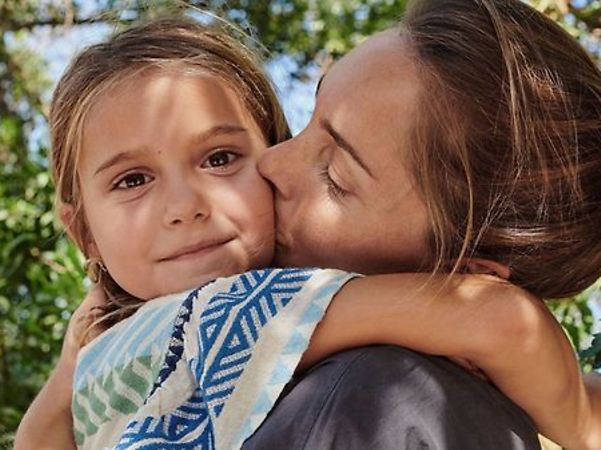 An adult hugs a child outdoors and kisses them on the cheek.