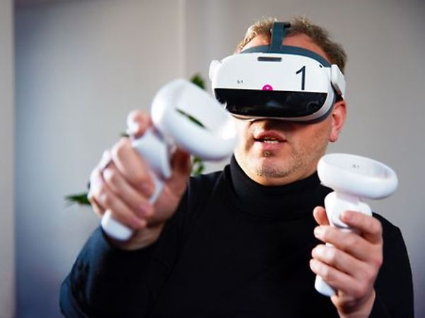 A person is wearing a virtual reality headset and holding two controllers in their hands.