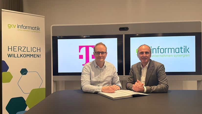 Two men are sitting in front of gkv-informatik and Telekom screens.