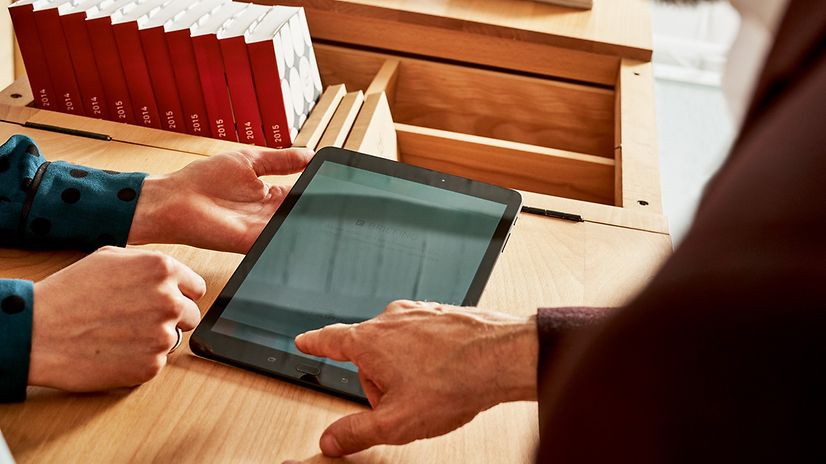 Two people are using a tablet together on a wooden table.