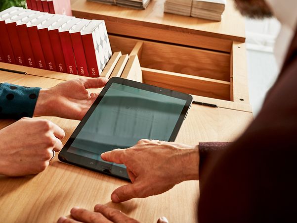 Two people are using a tablet together on a wooden table.