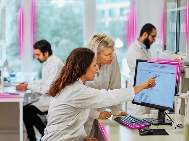 Researchers in the laboratory are looking at a diagram on a monitor together.