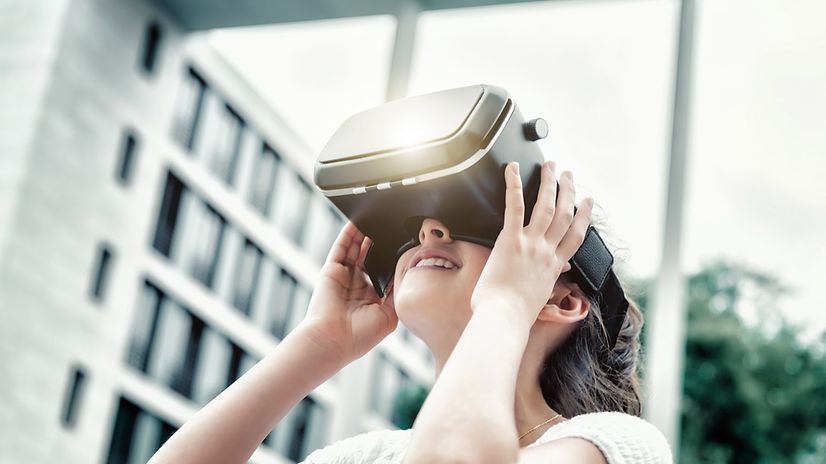 A schoolgirl is wearing VR glasses in front of a blurred school building.