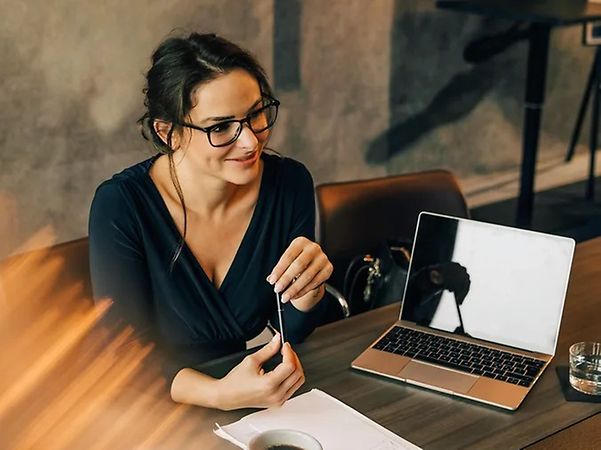 A woman is sitting at a table with a laptop and a pen.